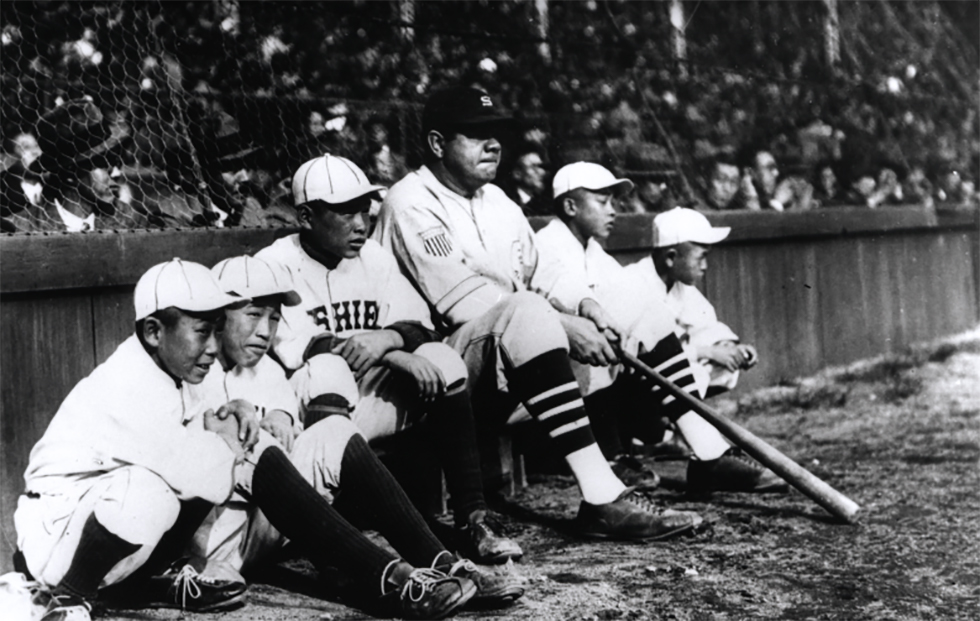 A young, black baseball player sits in the dugout during a